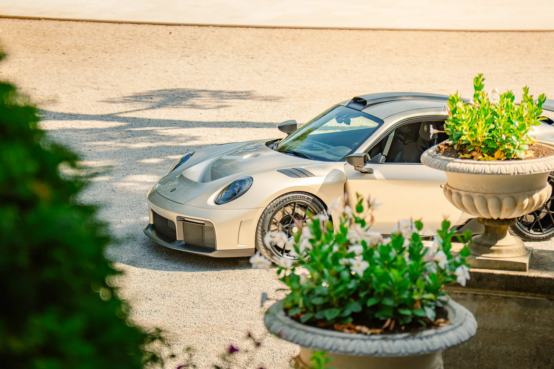 Porsche 911 argentée garée dans une allée fleurie