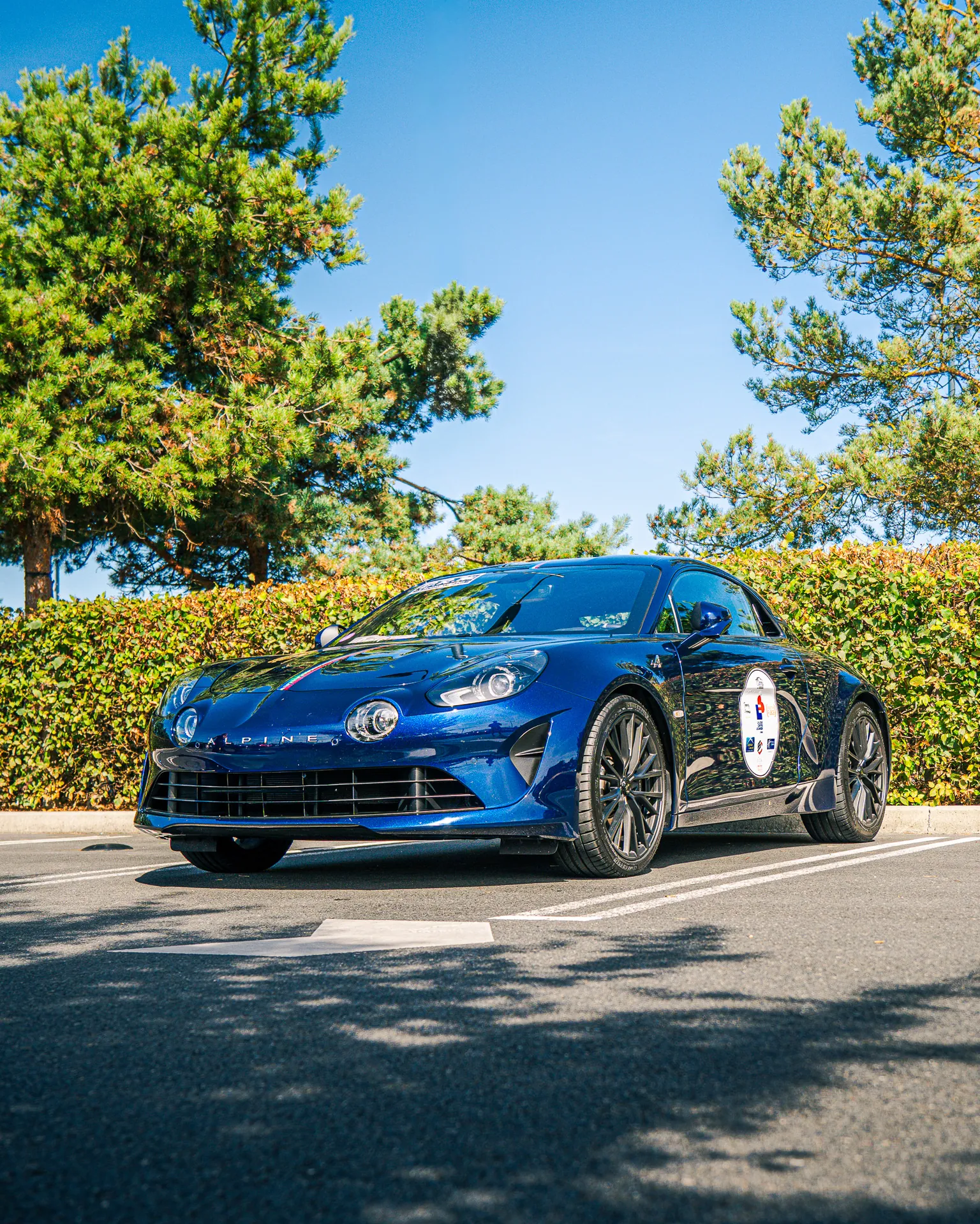 Alpine A110 bleue sur un parking ombragé
