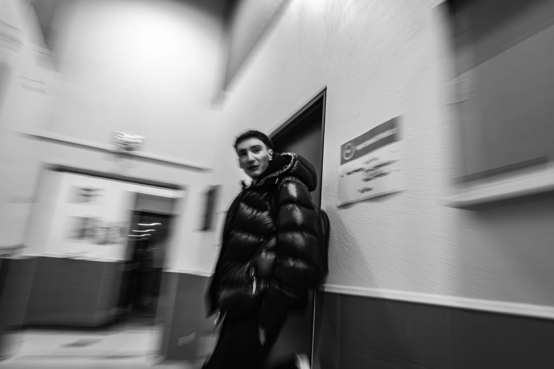 Jeune homme adossé à un mur dans un couloir, noir et blanc avec filé
