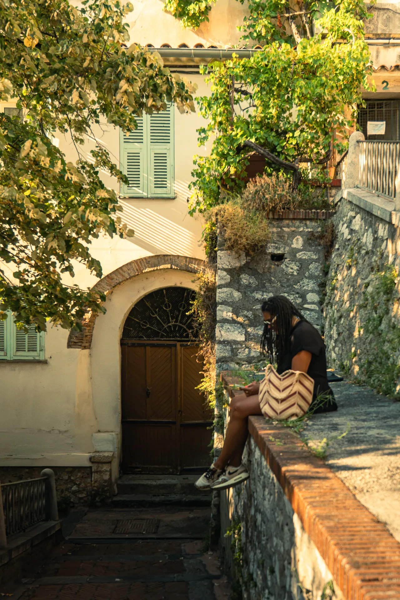 Ruelle de village avec une passante assise sur un muret