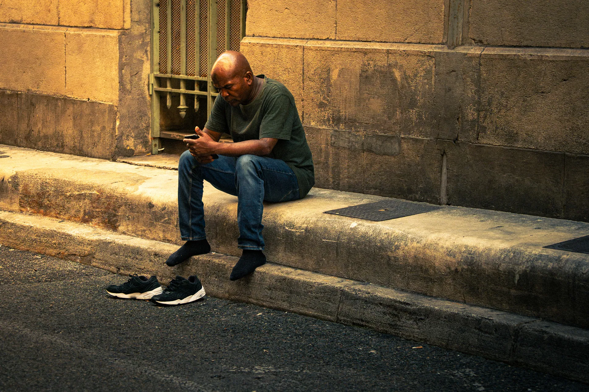 Homme assis sur un trottoir consultant son téléphone, lumière de fin de journée