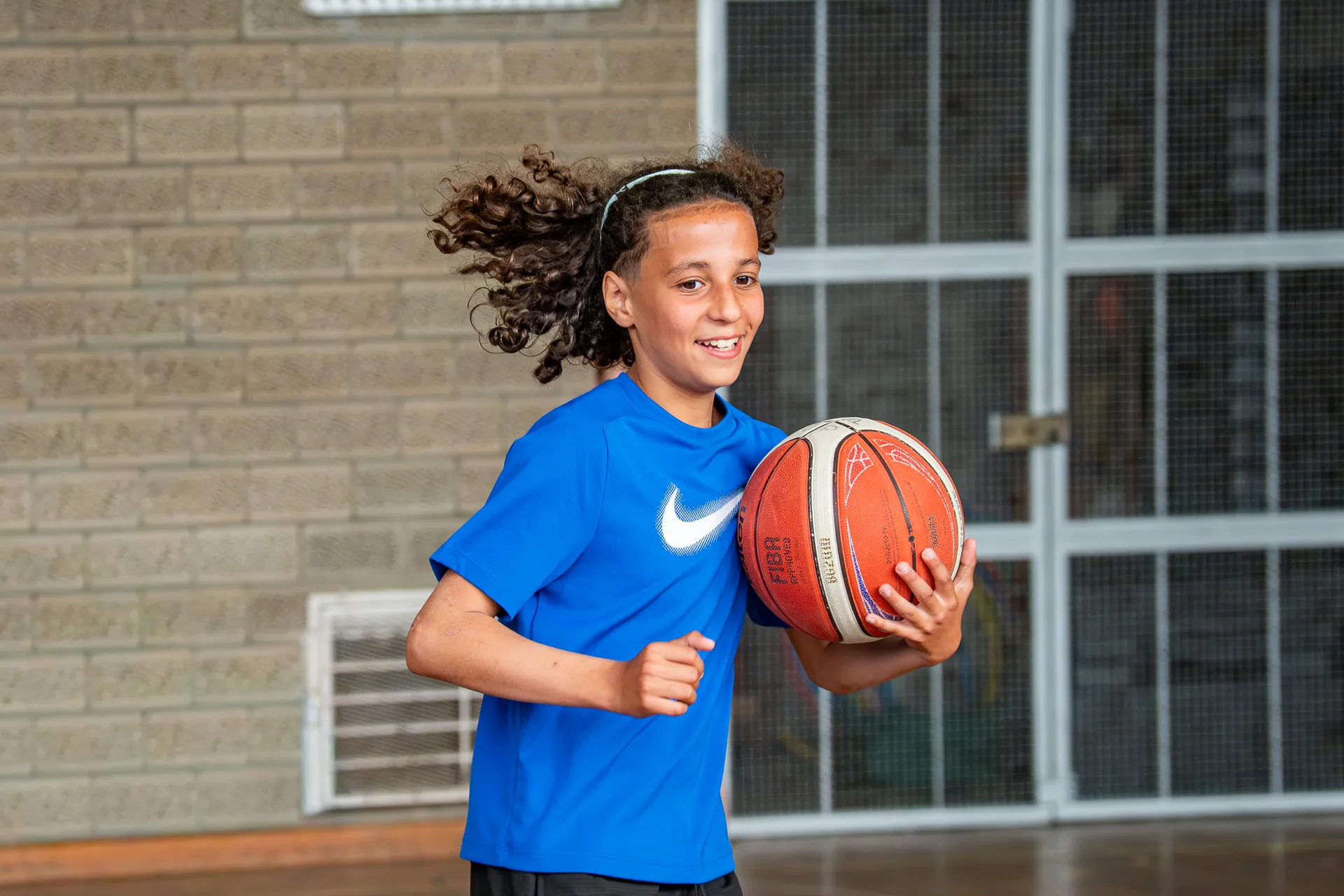Jeune basketteur souriant avec un ballon devant une grille de gymnase