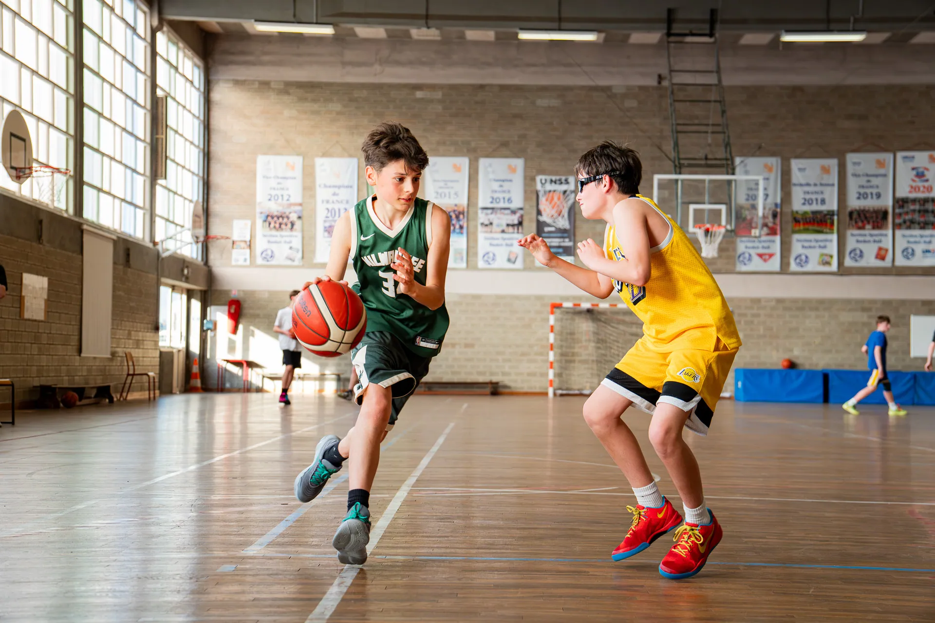 Duel entre deux jeunes basketteurs, dribble face à un défenseur en jaune