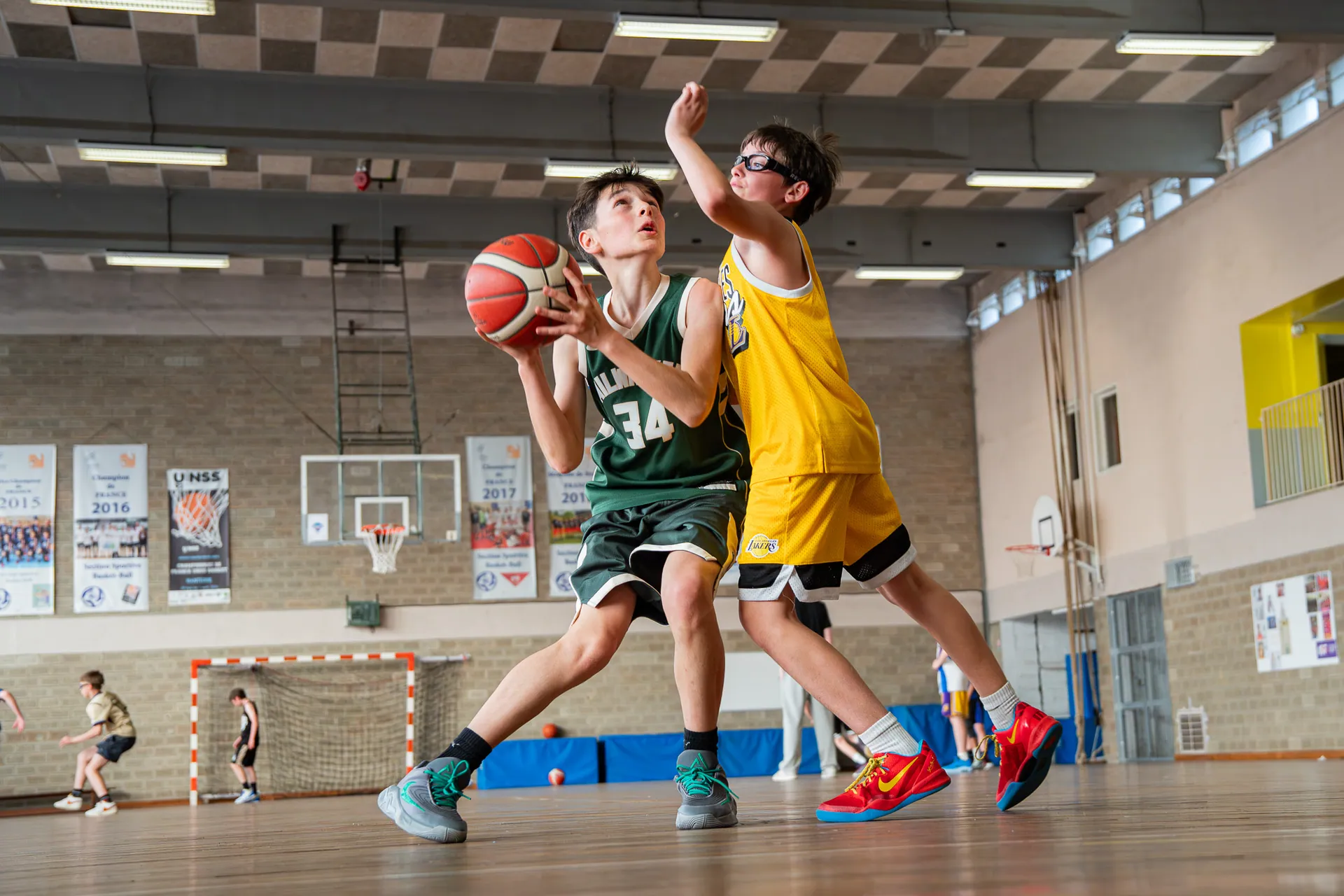 Jeune basketteur montant au panier face à un contreur en jaune