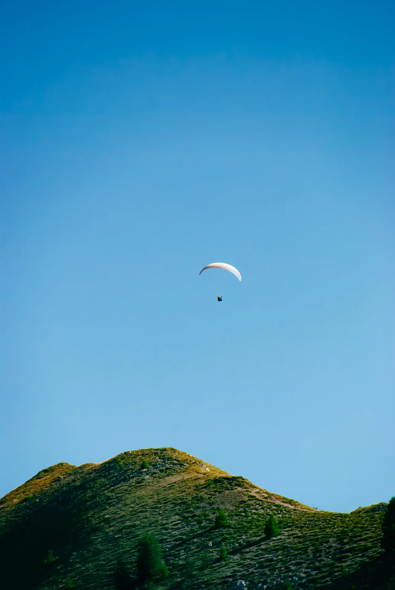 Parapente dans un ciel bleu au-dessus d’une colline verte