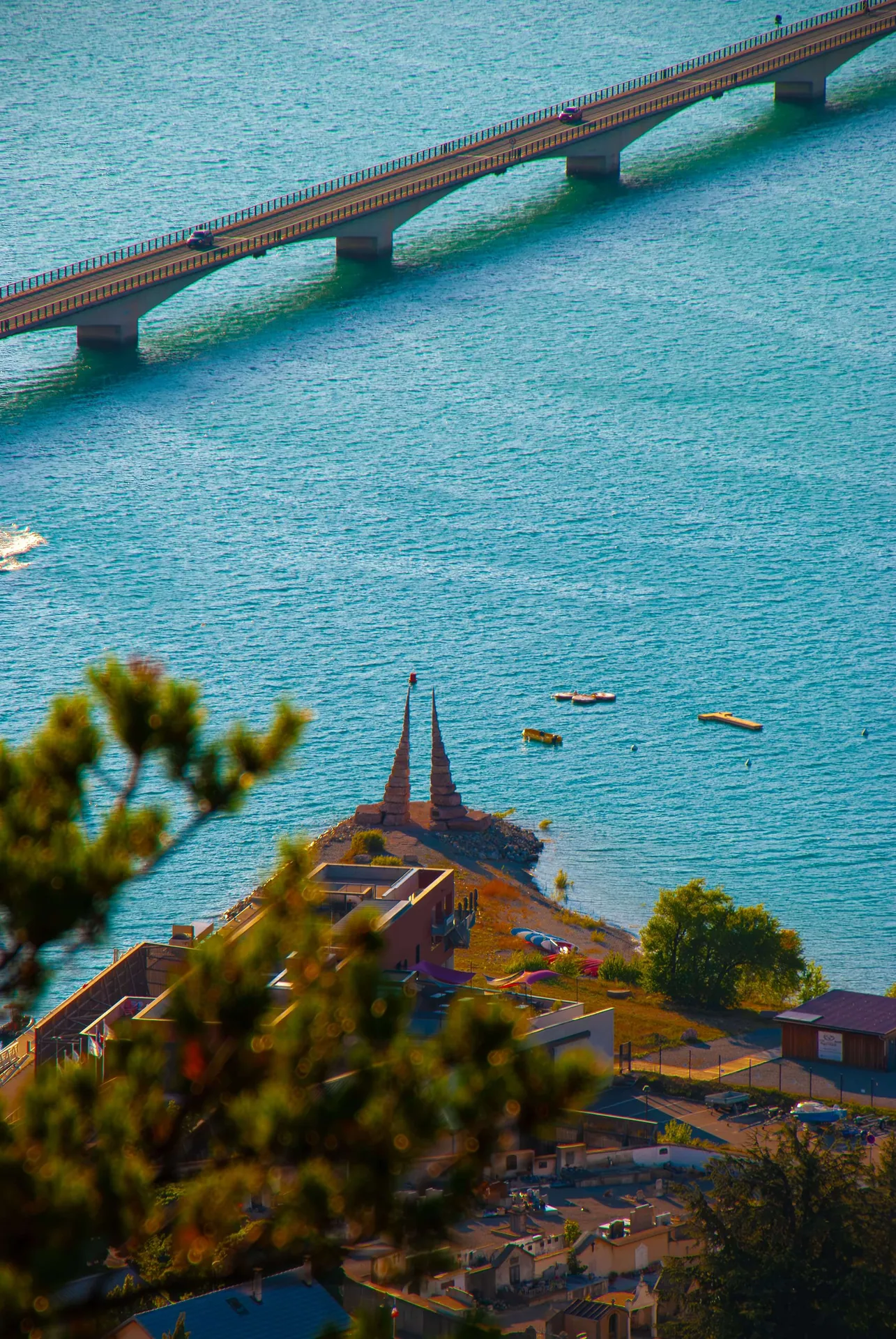 Pont traversant un lac turquoise, vu depuis une colline boisée